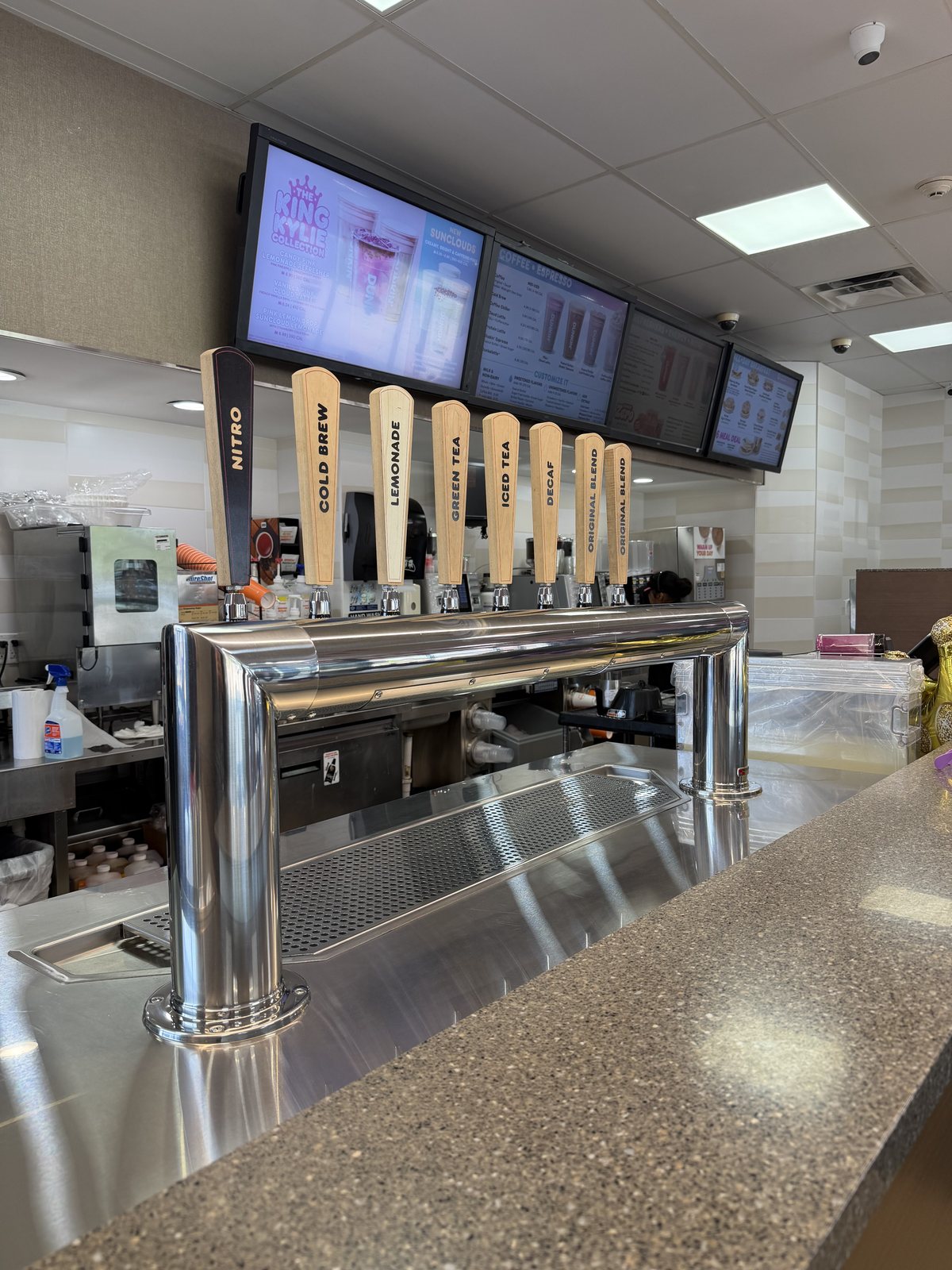 The cold brew, nitro, and iced tea tap wall at a PPP Donuts Network Dunkin', with the digital menu boards above