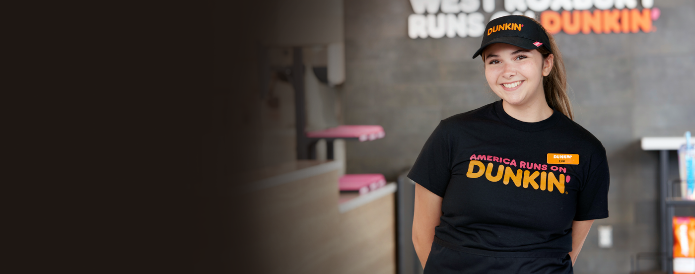 A smiling PPP Donuts Network crew member behind the counter at Dunkin'