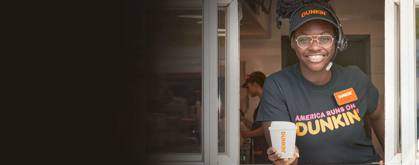A PPP Donuts Network crew member smiling as she hands an order through the drive-thru window